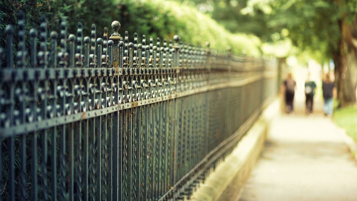 A long black ornamental metal fence beside a sunny park path