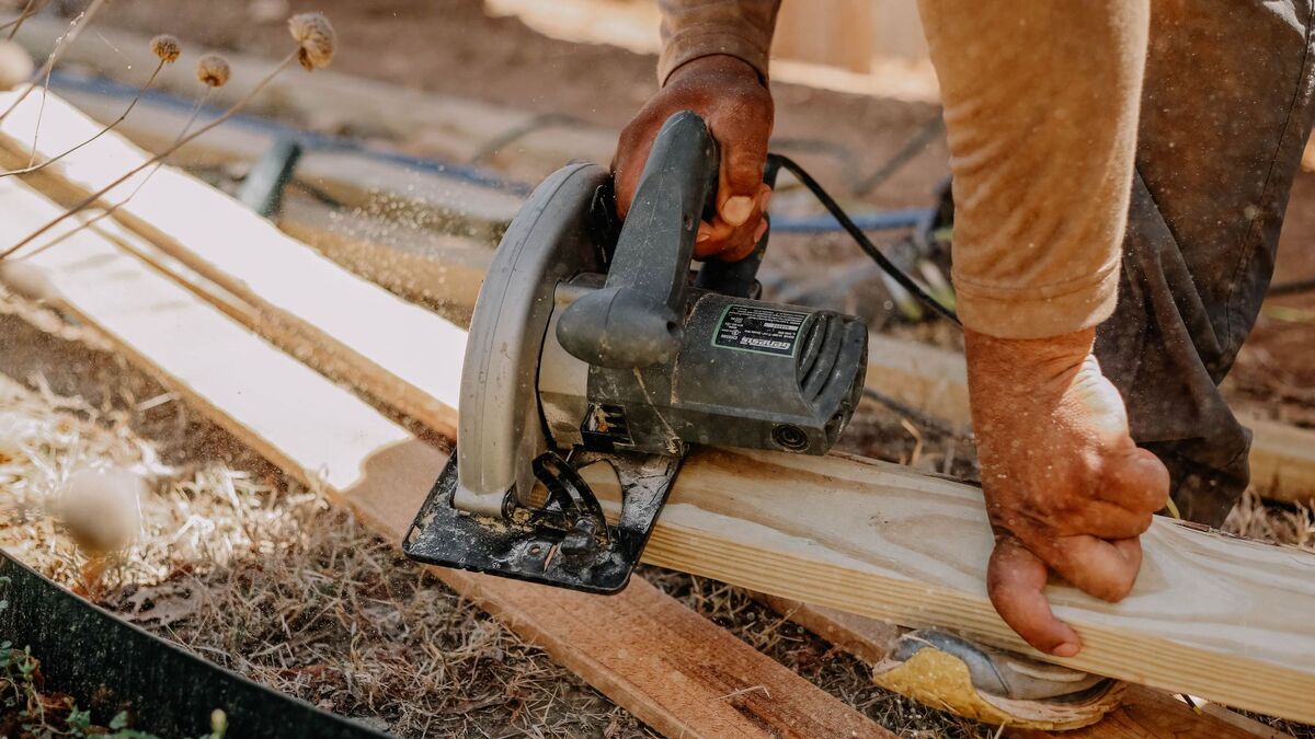 A worker cutting a fence board with a circular saw outdoors