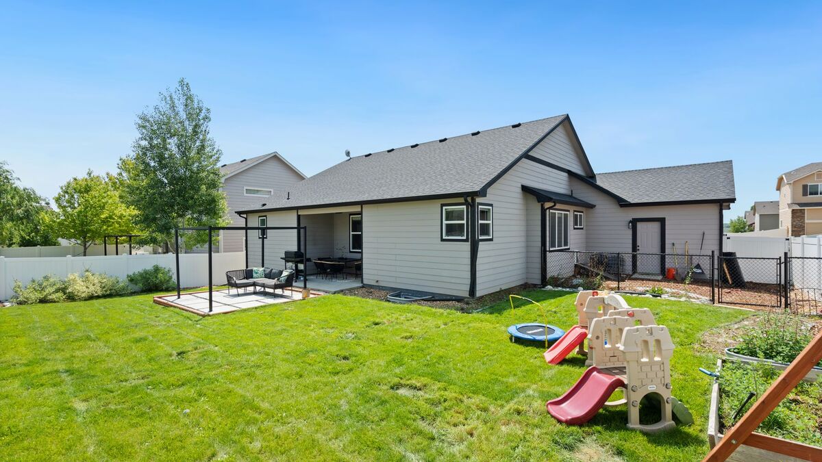 A backyard lawn with a play set, a single-story house and a white vinyl fence along the yard