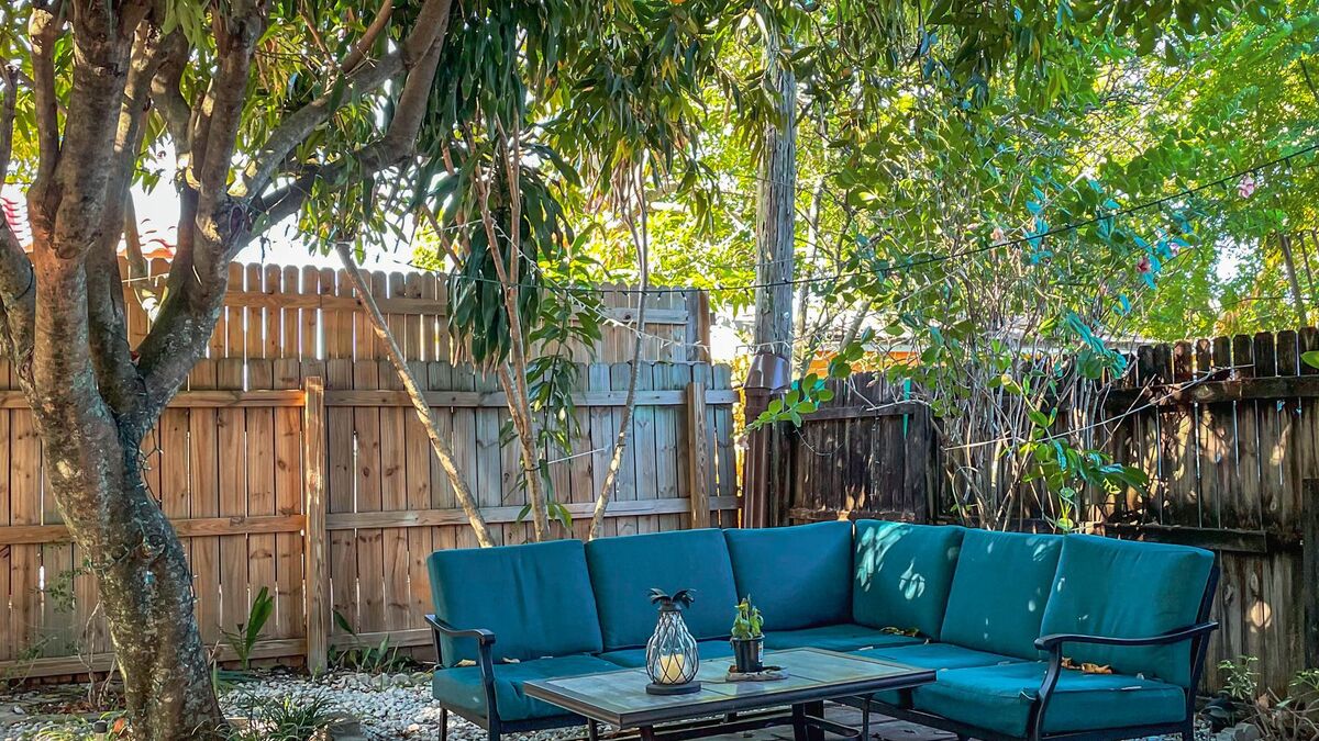 A backyard patio with a blue outdoor sectional in front of a wood privacy fence